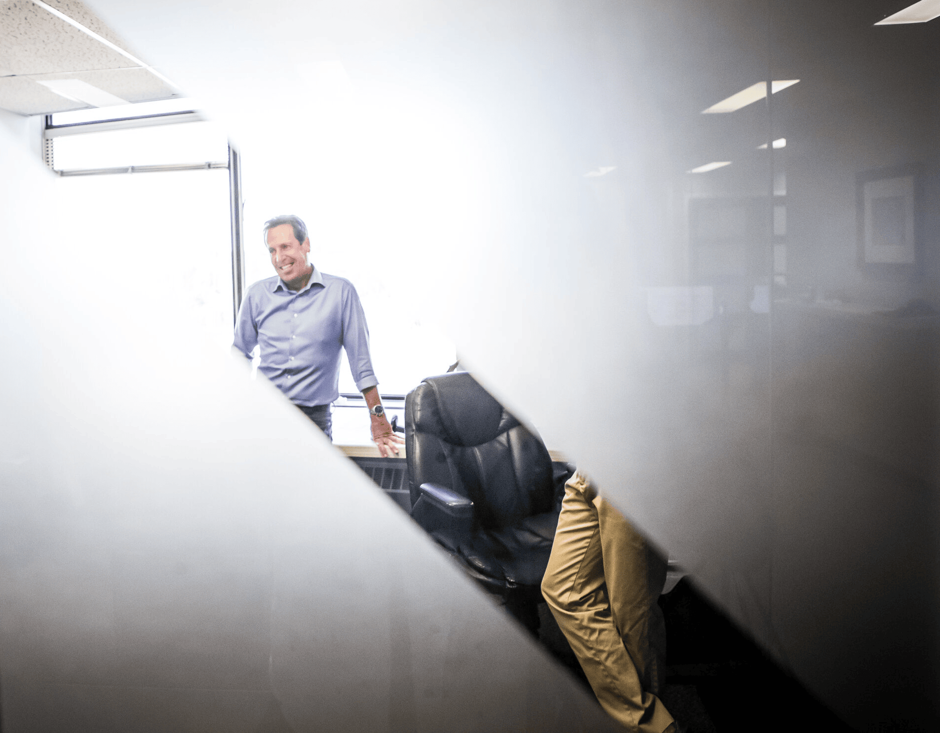 View through a glass door of two men in an office, one smiling, representing LAN Solutions’ people-first culture and positive workplace relationships